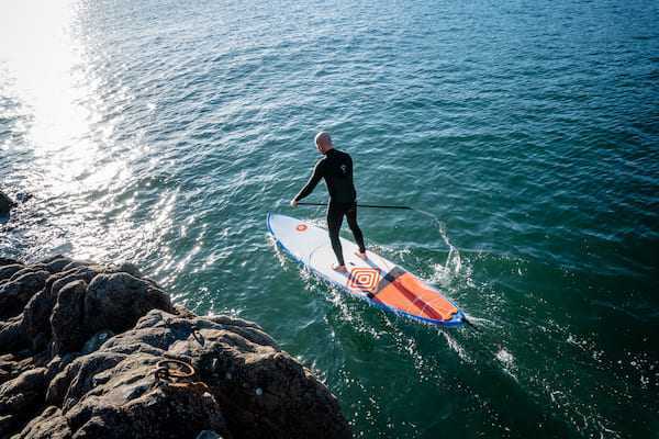 Un homme en combinaison de plongée se tient debout sur une planche à rame